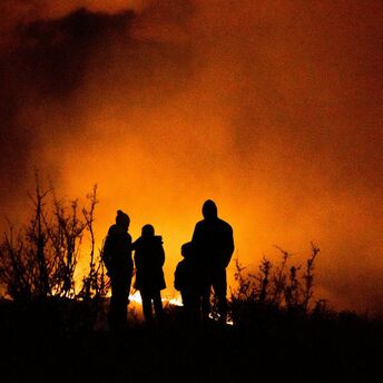 People standing near a large wildfire at night