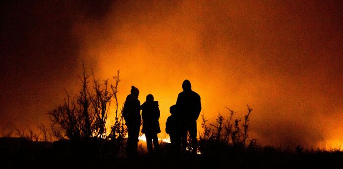 People standing near a large wildfire at night