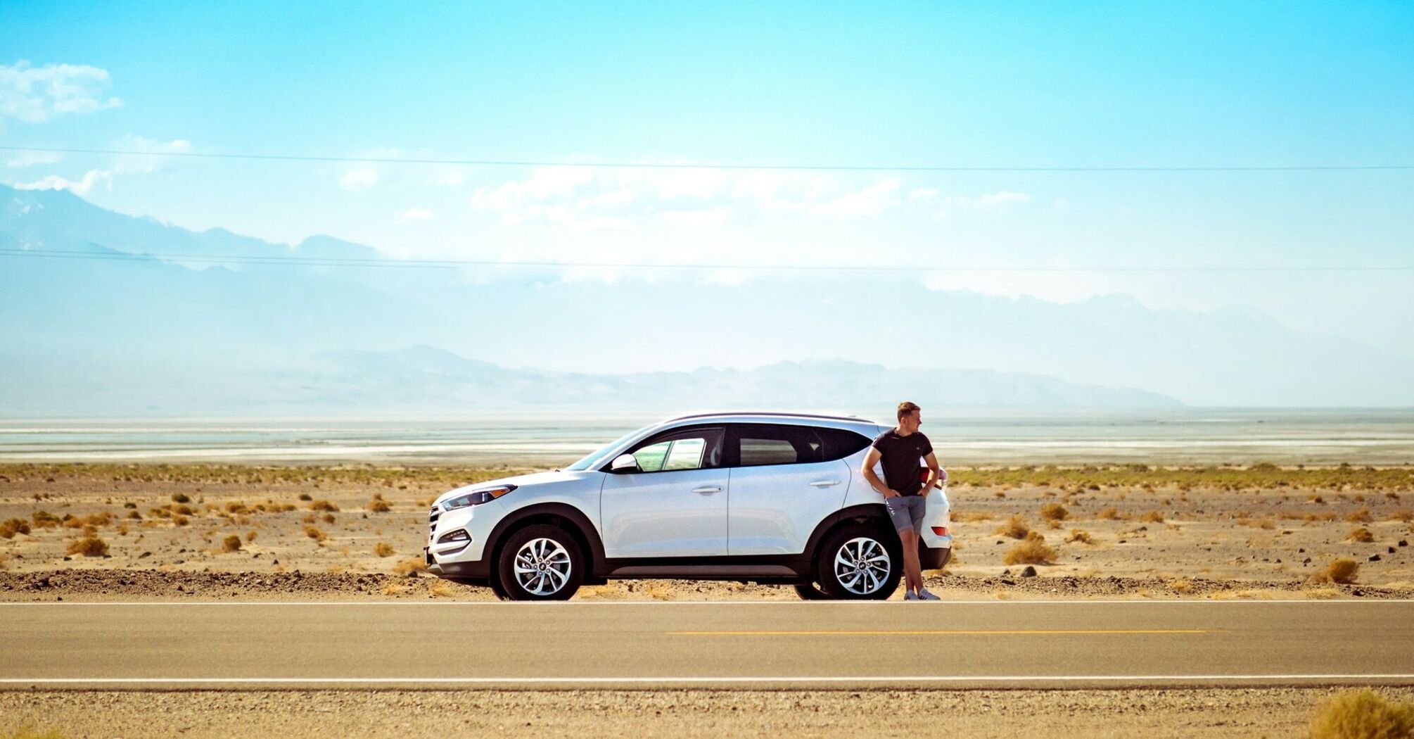 Driver standing beside a rental car on a road